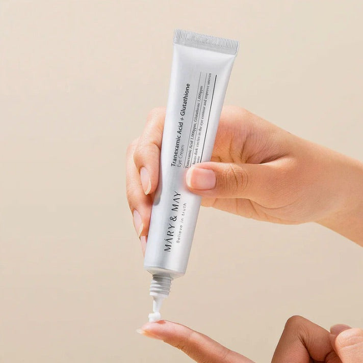 Hand holding a tube of Mary & May skincare product against a beige background