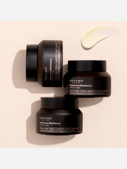 Three black cosmetic jars with 'Mary & May' branding on a beige background