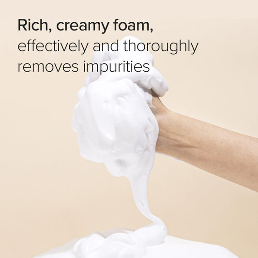 Hand holding a lathered bar of soap with text about its cleansing properties on a beige background