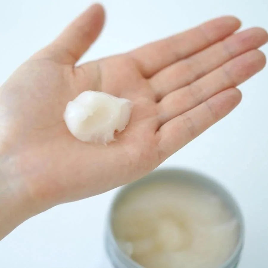 Hand holding a small amount of cream with a container of cream in the background