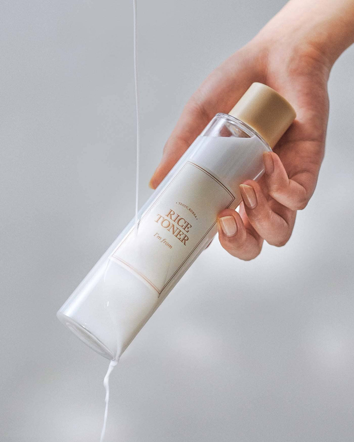 Hand holding a bottle of rice toner with a neutral background