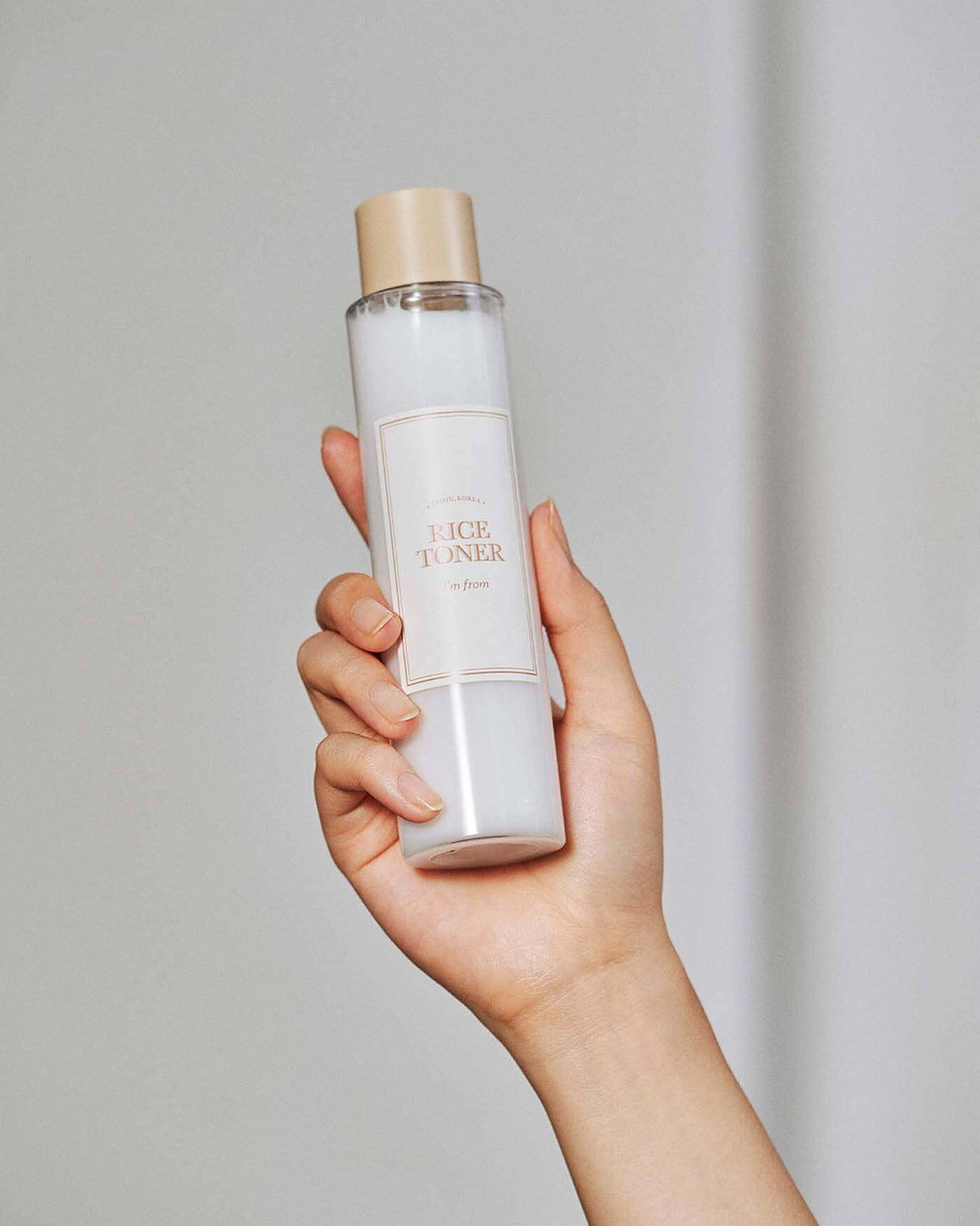 Hand holding a bottle of face toner against a plain background