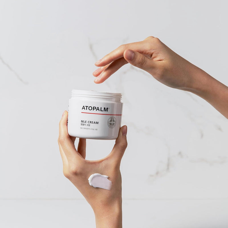 Person holding a jar of Atopalm MLE Cream with a white background