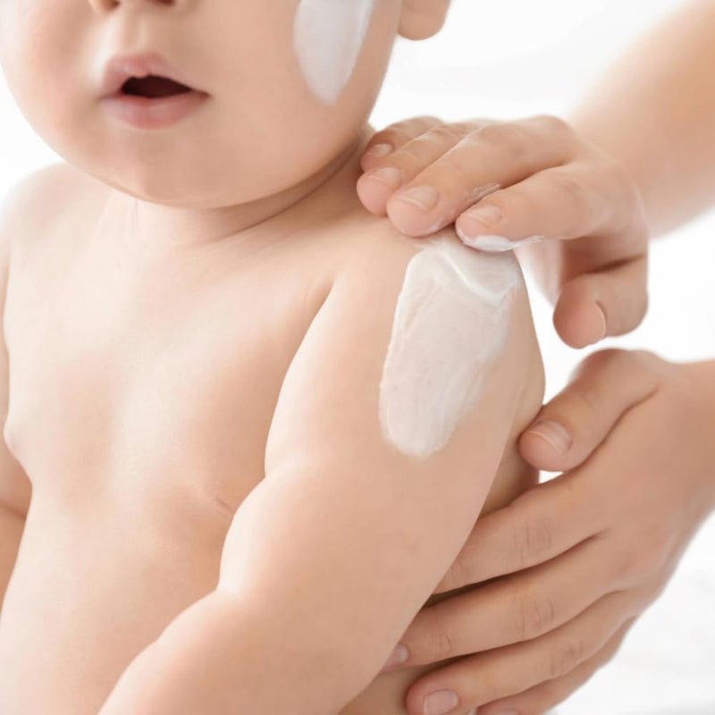Baby with a white cream applied to its arm, held by an adult hand.