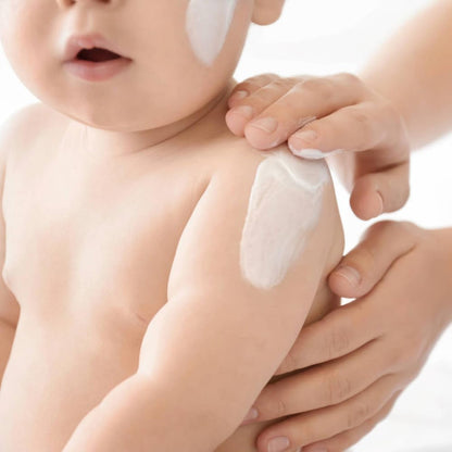 Baby with a white cream applied to its arm, held by an adult hand.