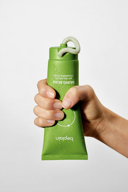 Hand holding a green bottle with a white cap against a light gray background