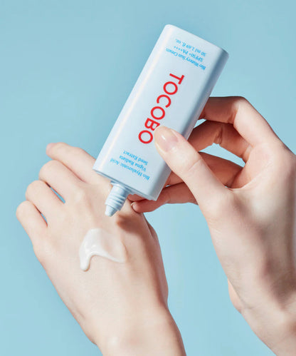 Hand applying a white cream to another hand with a blue background