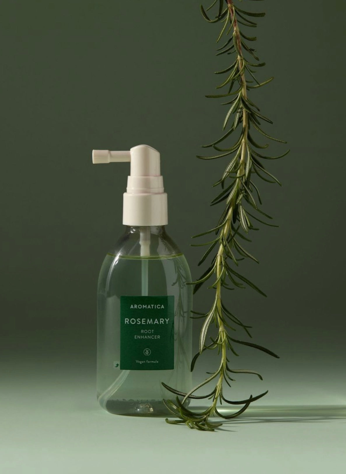 Glass bottle with pump and rosemary plant on a green background