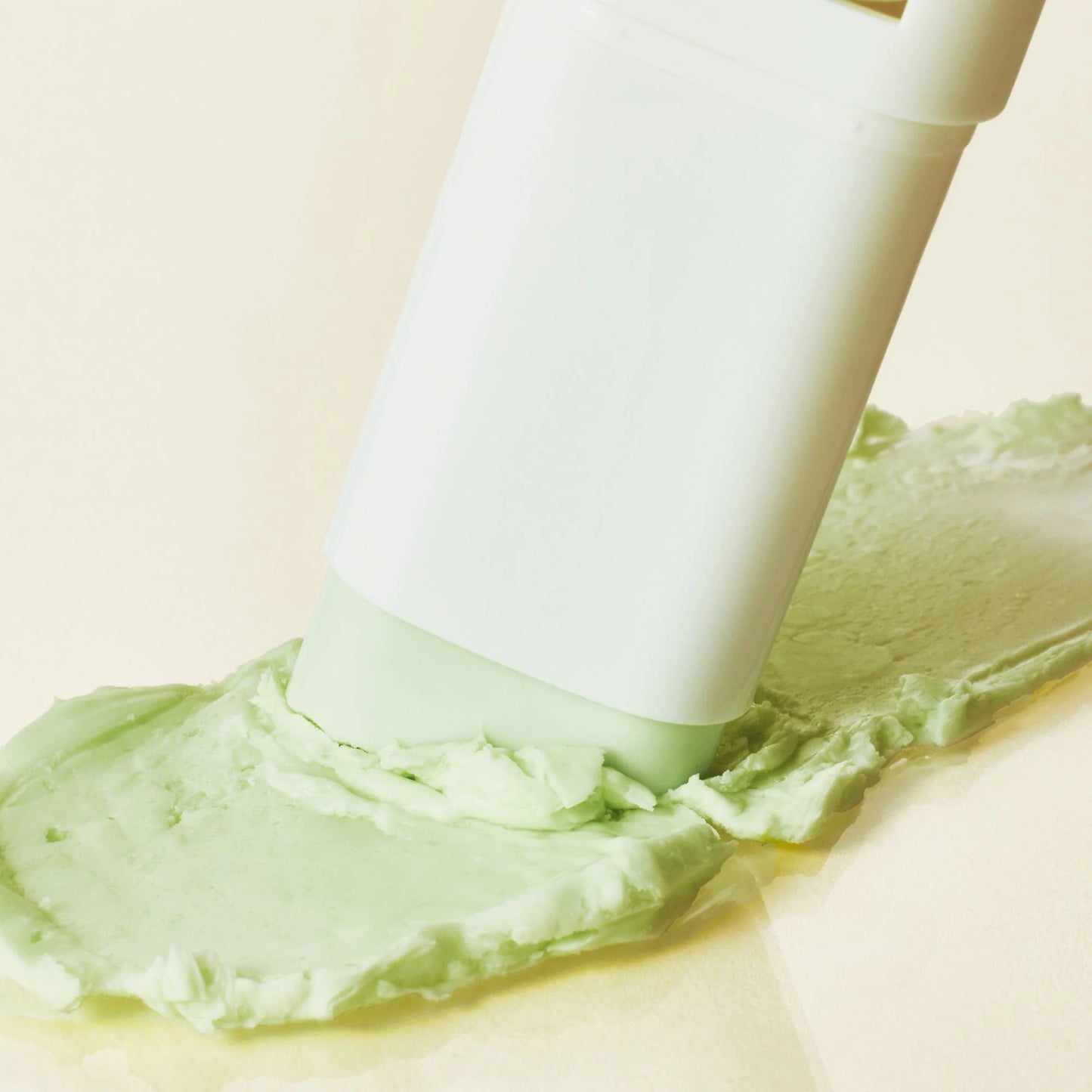 White spatula spreading green cream on a beige background